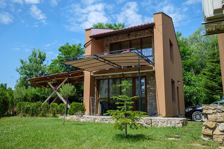 Two-story villa with a sunny veranda and stone details, surrounded by greenery at Villa Zora holiday complex, Shkorpilovtsi