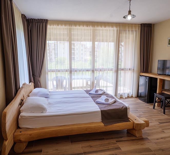 Sunny bedroom with a double wooden bed, balcony view, TV, and mini fridge in a villa at Villa Zora holiday complex.